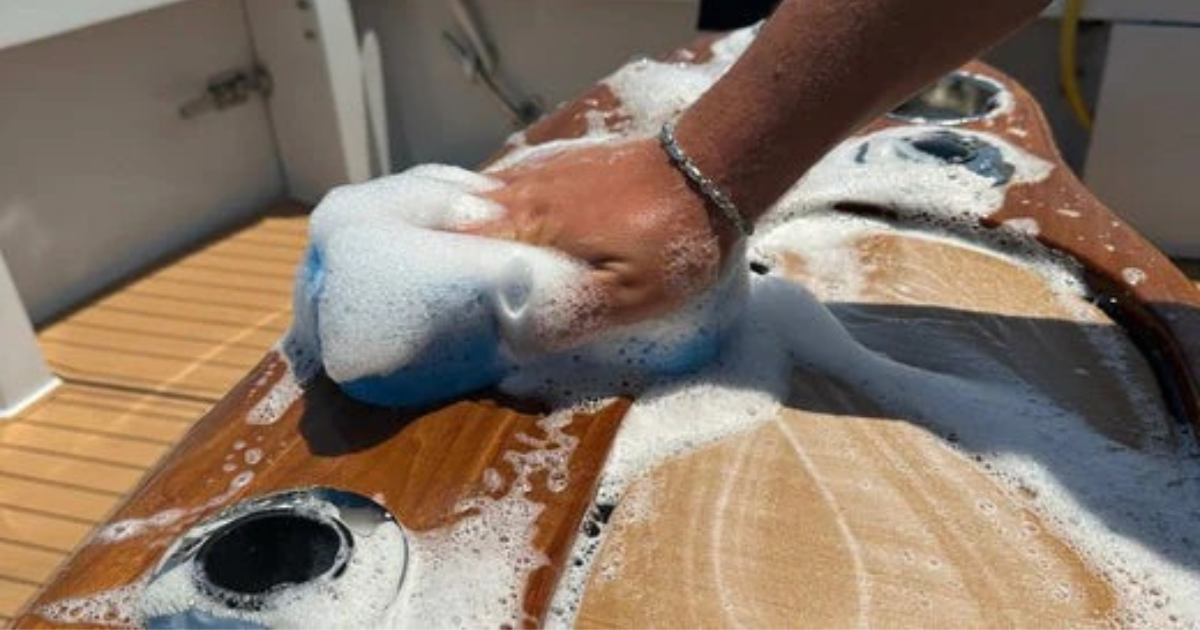 Limpeza do deck de teca no interior de barco com esponja e shampoo náutico — manutenção profissional de embarcação