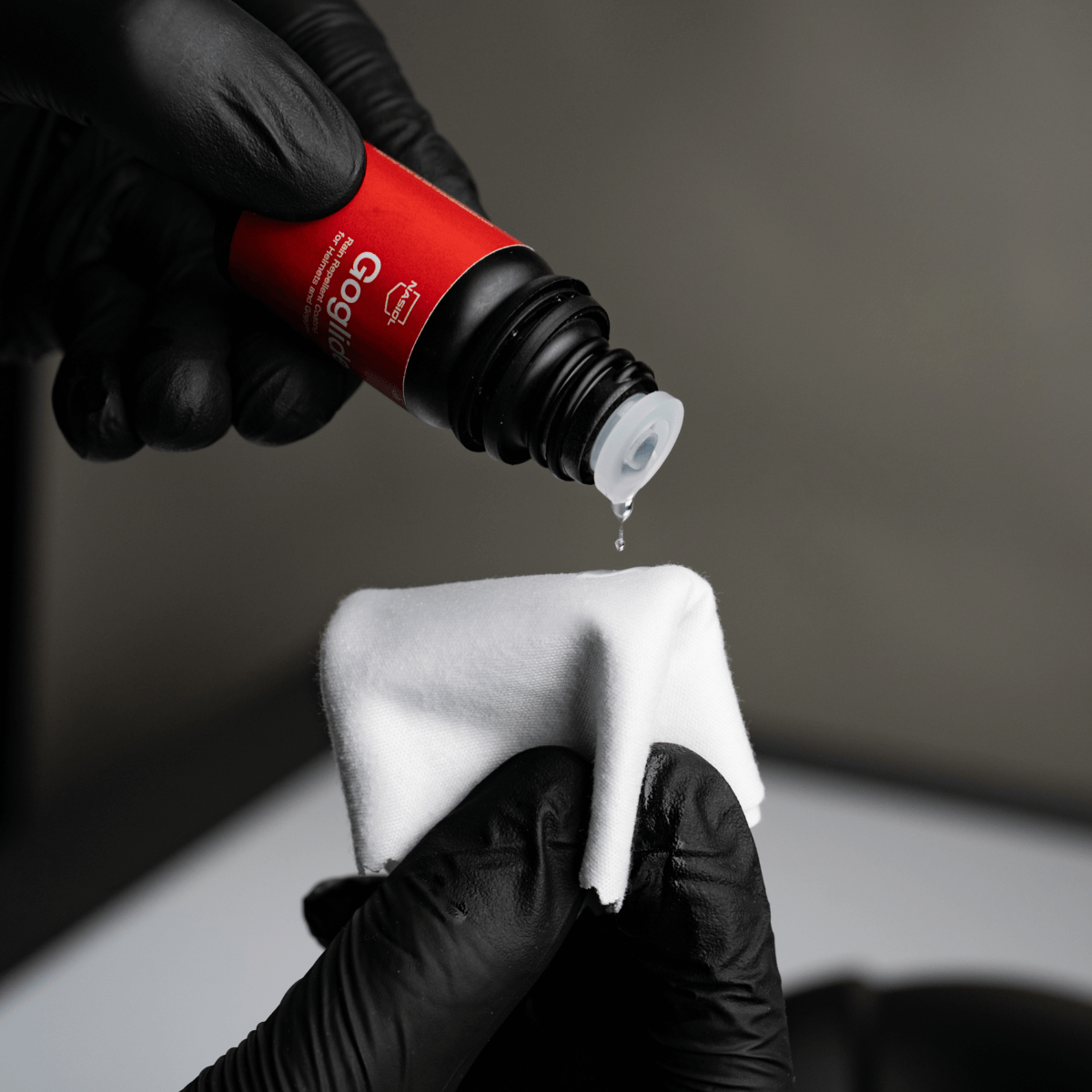 Aplicação de gotas de Nasiol Goglide num pano de camurça branco com luvas pretas